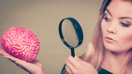 Blonde woman holding magnifying glass investigating something and looking closely at fake brain.の写真素材