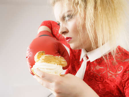 Dieting, weight loss concept. Funny blonde woman holding yummy choux puff cake with whipped cream...