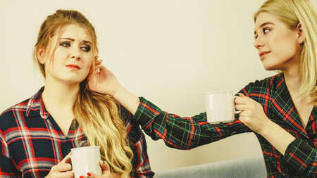 Two women spending time together on sofa drinking tea. Female complaining, the other one comforting...