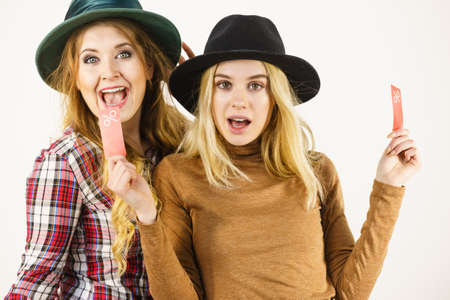 Female friends on shopping showing tag with sale percentage sign enjoying cheap clothing.
