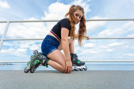 Unrecognizable woman putting on roller skates. Female being sporty having fun during summer in city