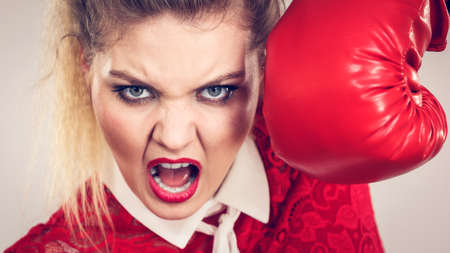 Sporty angry determined woman wearing red boxing gloves, fighting. Studio shot on dark background.の写真素材