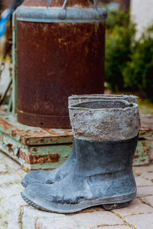 Village detailed objects concept. Very old wellingtons and copper bottle standing outside