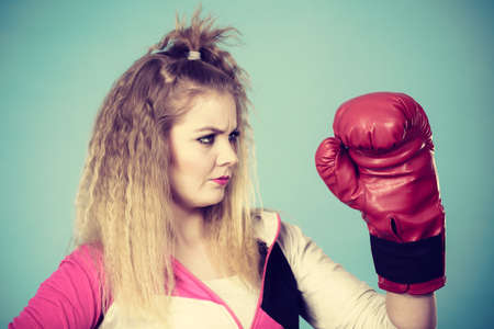Cute blonde girl female boxer with big fun red gloves playing sports boxing studio shot on blueの写真素材