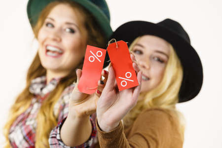 Female friends on shopping showing tag with sale percentage sign enjoying cheap clothing.の写真素材