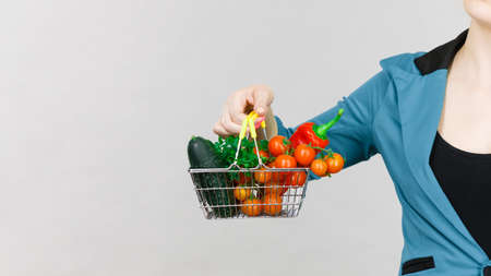 Lose weight, buying healthy food, vegetarian products. Woman hand holding little shopping basket with high fibre red green vegetables inside, on greyの写真素材