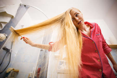 Woman wearing pajamas in bathroom having fun while brushing her long blonde hair, windblown hairdo, shot from bottom.の写真素材