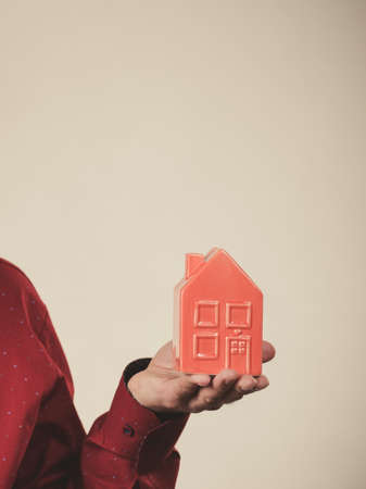 Unrecognizable man holding small red house model on palm of hand. Real estate concept.の写真素材
