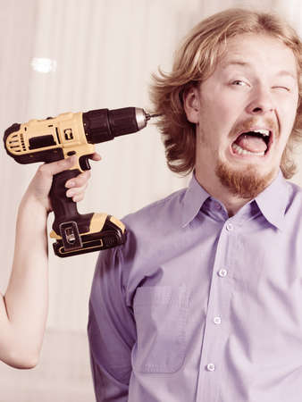 Man being scared of unrecognizable person holding electric drill. Guy having head ache
