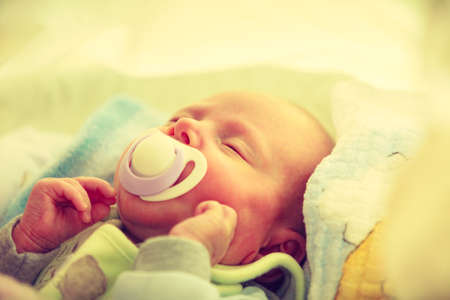 Infant care, beauty of childhood concept. Little newborn baby sleeping calmly in bed with teat in...