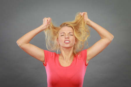 Haircare, health problem concept. Frustrated, depressed woman holding and pulling out her damaged blonde hair with closed eyes.の写真素材