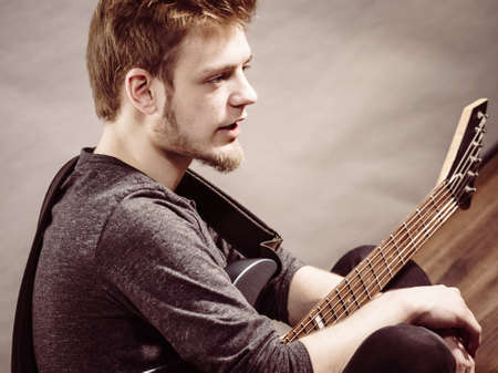 Young bearded man with electric guitar. Adult person is holding instrument and playing. Hobby, music concept, on greyの写真素材