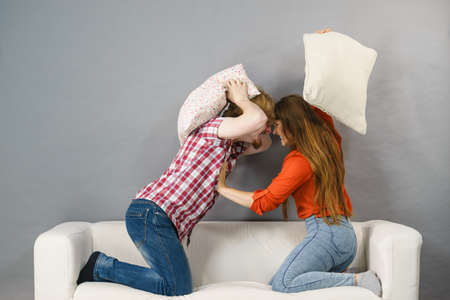 Angry couple having pillow fight. Brother and sister having conflist on sofa.