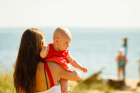 Summer family recreation concept. Mother holding and playing with little baby on beach during...