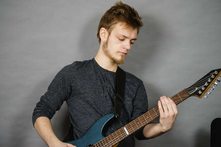 Young bearded man with electric guitar. Adult person is holding instrument and playing. Hobby, music...