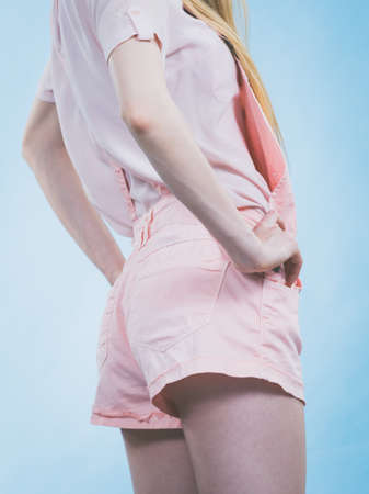 Unrecognizable woman back view. Female wearing cute outfit, pink dungarees, white tshirt. Studio shot on blue backgroundの写真素材