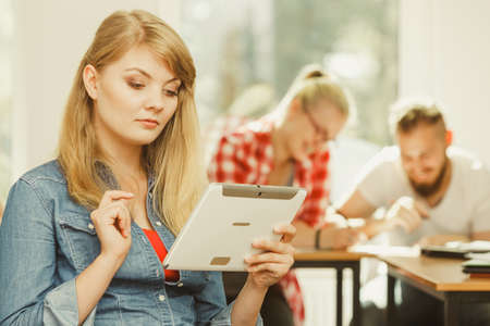 Education, high school, digital online learning concept - student girl with tablet pc computer sitting in front of students her group mates in classroomの写真素材