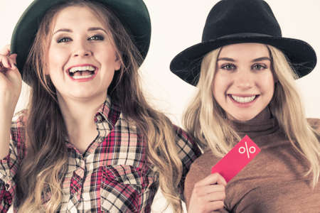 Female friends on shopping showing tag with sale percentage sign enjoying cheap clothing.の写真素材