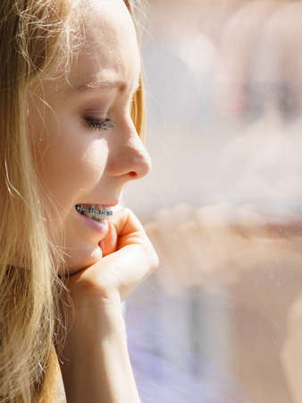 Smiling young woman teenage girl sitting on window sill, energizing morning, relaxing having good...