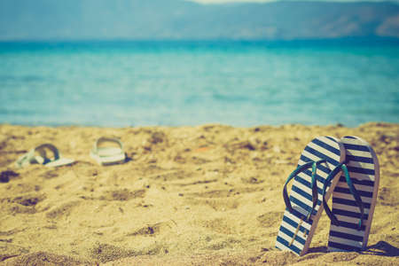 Blue and white flip flops on sand beach during summer time weather.の写真素材