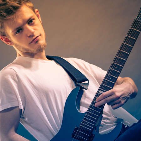 Young bearded man with electric guitar. Adult person is holding instrument and playing. Hobby, music concept, on greyの写真素材