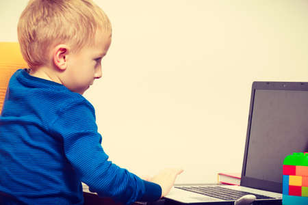 Children and technology, spending free time online concept. Little boy using laptop computer playing...