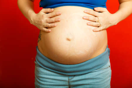 Parenthood, waiting for baby concept. Adult woman showing her big pregnant belly. Indoor shot on red...