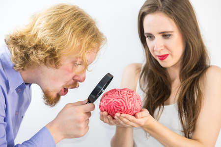 Woman and man looking at human brain model using magnifying glass for closer look. Couple being inspired, doing experiment discovering things.の写真素材
