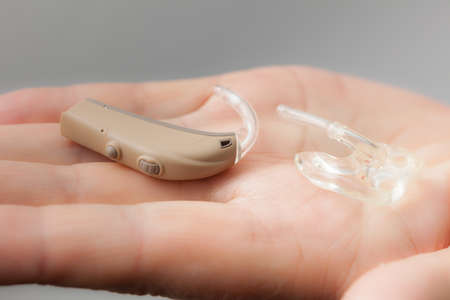 Closeup senior woman with electronic hearing aid in her hand. Health care, hear disorder, device for the deaf.の写真素材