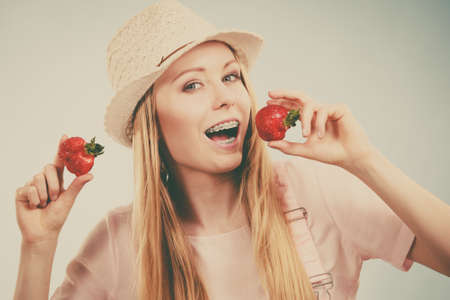 Happy cheerful teenage young woman ready for summer wearing pink outfit and sun hat holding sweet fruit red strawberriesの写真素材