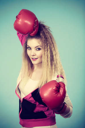 Funny blonde girl female boxer in big fun red gloves playing sports boxing studio shot on blue
