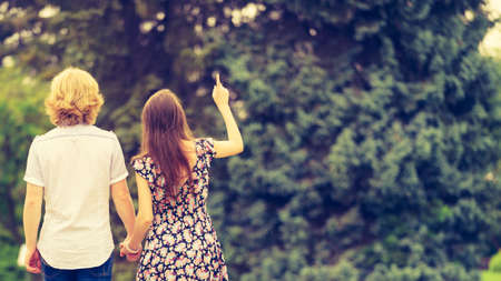 Man and woman walking in public park having fun during summer warm weather wearing fashionable outfits. View from back.の写真素材