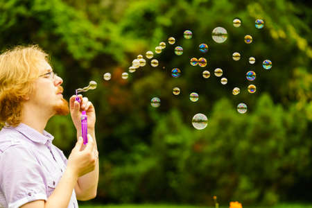 Happy young adult man blowing soap bubbles in nature green spring park.の写真素材