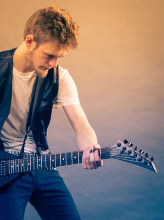 Young bearded man with electric guitar. Adult person is holding instrument and playing. Hobby, music concept, on greyの写真素材