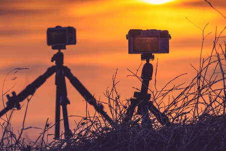 Professional camera on tripod taking picture film video of sunrise over meadow field, Greeceの写真素材