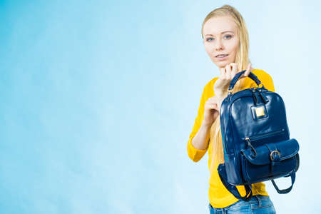 Blonde teenage girl going to school or college wearing stylish backpack. Outfit trendy accessories. On blueの写真素材