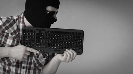 Crazy hacker man. Unrecognizable guy wearing black balaclava holding computer keyboard. Hate speech...