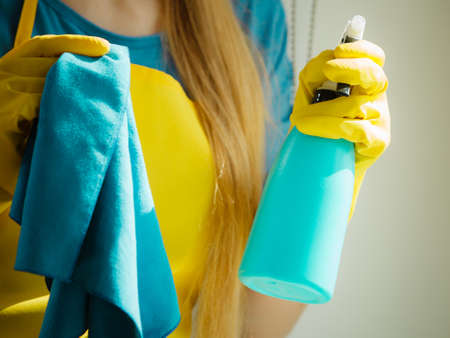 Female hand in yellow gloves cleaning window with blue rag and spray detergent. Spring cleanup,...
