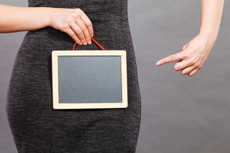 Feminine body problems concept. Woman holding blank black board on crotch, grey background.の写真素材