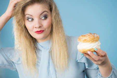 Sweet food and happiness concept. Funny joyful blonde woman holding yummy choux puff cake with...