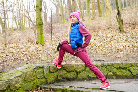 Sport and recreation. Fit slim sporty teen girl stretching warming up outdoor in park. Woman...