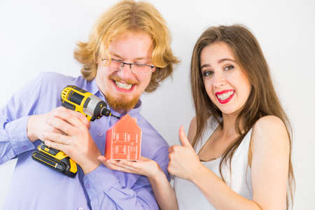 Happy couple is about to do home renovation. Man and woman holding house model and drillの写真素材
