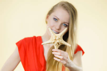 Woman holding starfish shell wearing red dress having fun, smiling face expression.の写真素材