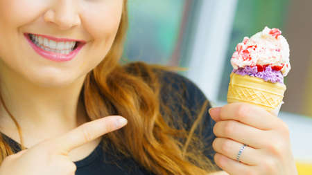 Happy funny young woman with long brown hair eating ice cream having fun.の写真素材