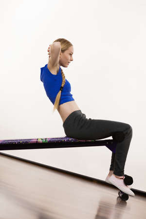 Young teenage woman training on bench for sit ups at home. Being fit and healthy, stomach muscles workout.の写真素材