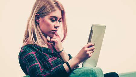 Young teenage woman using tablet while sitting on sofa and relaxing surfing on internetの写真素材