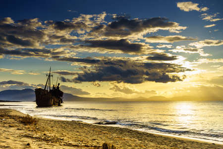 An old abandoned shipwreck, wrecked boat sunken ship stand on beach coast. Scenic sunset skyの写真素材