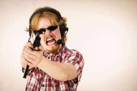 Nerd geek young adult man playing on the video console holding gun wearing headphones with microphone. Gaming gamers concept.の写真素材