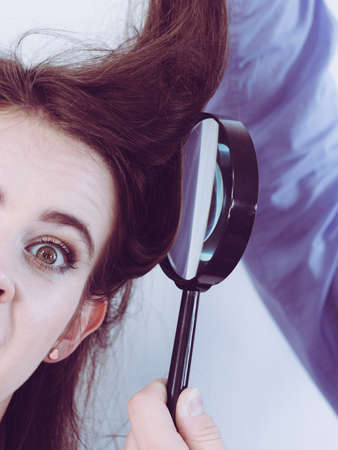 Person looking at woman hair roots using magnifying glass. Female being scared or worried.