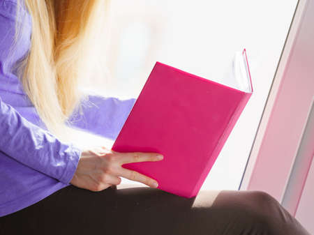 Leisure, literature and people concept. Young woman teen girl reading book at home while sitting on...